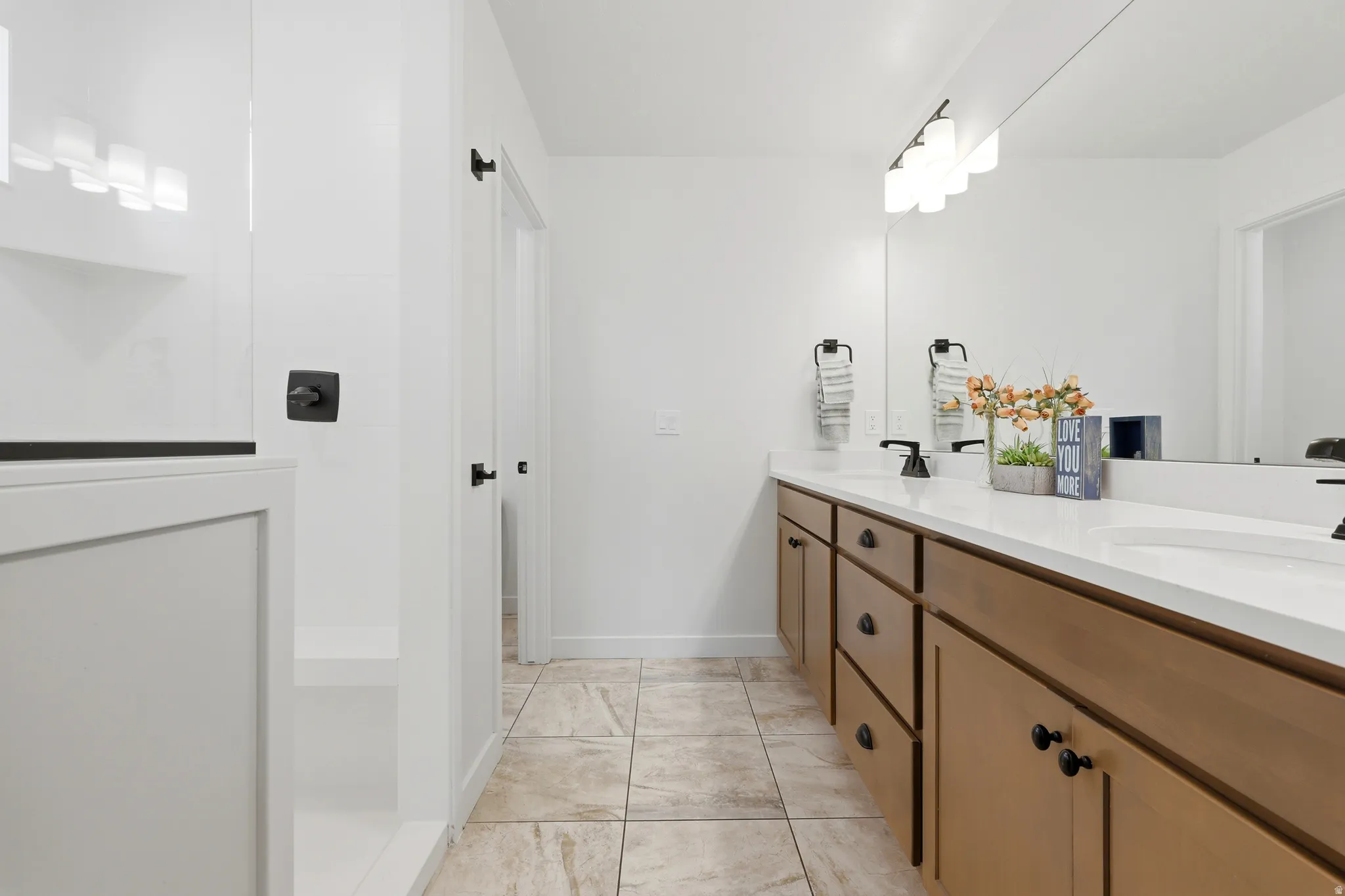 Dual vanity with wood-finish cabinetry, white countertops, and matte black hardware