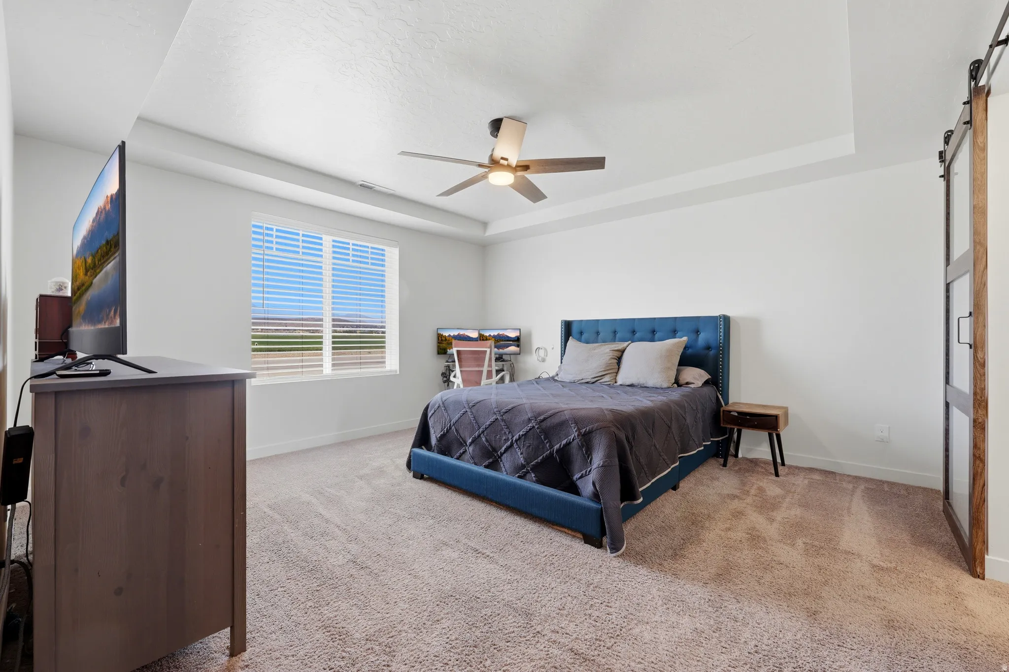 Spacious bedroom featuring a tray ceiling, ceiling fan, and carpeted flooring