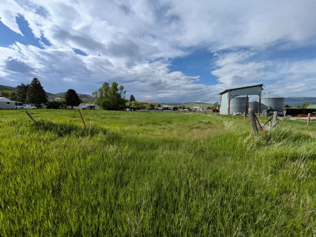 Expansive grassy lot featuring a distant mountain backdrop and agricultural structures