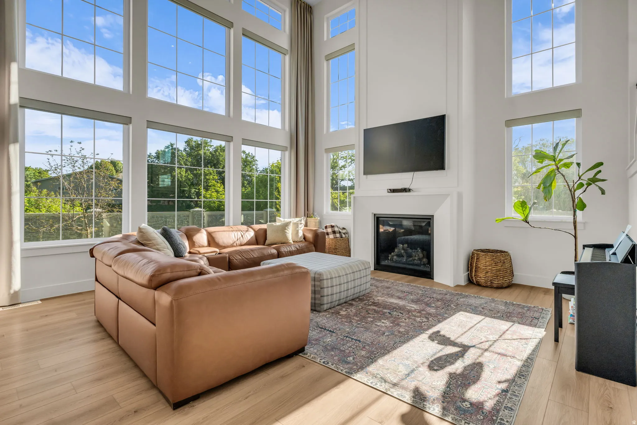 Two-story living area featuring tall windows with grid detailing, wood-finish flooring, a contemporary fireplace with a white mantel, and high ceilings