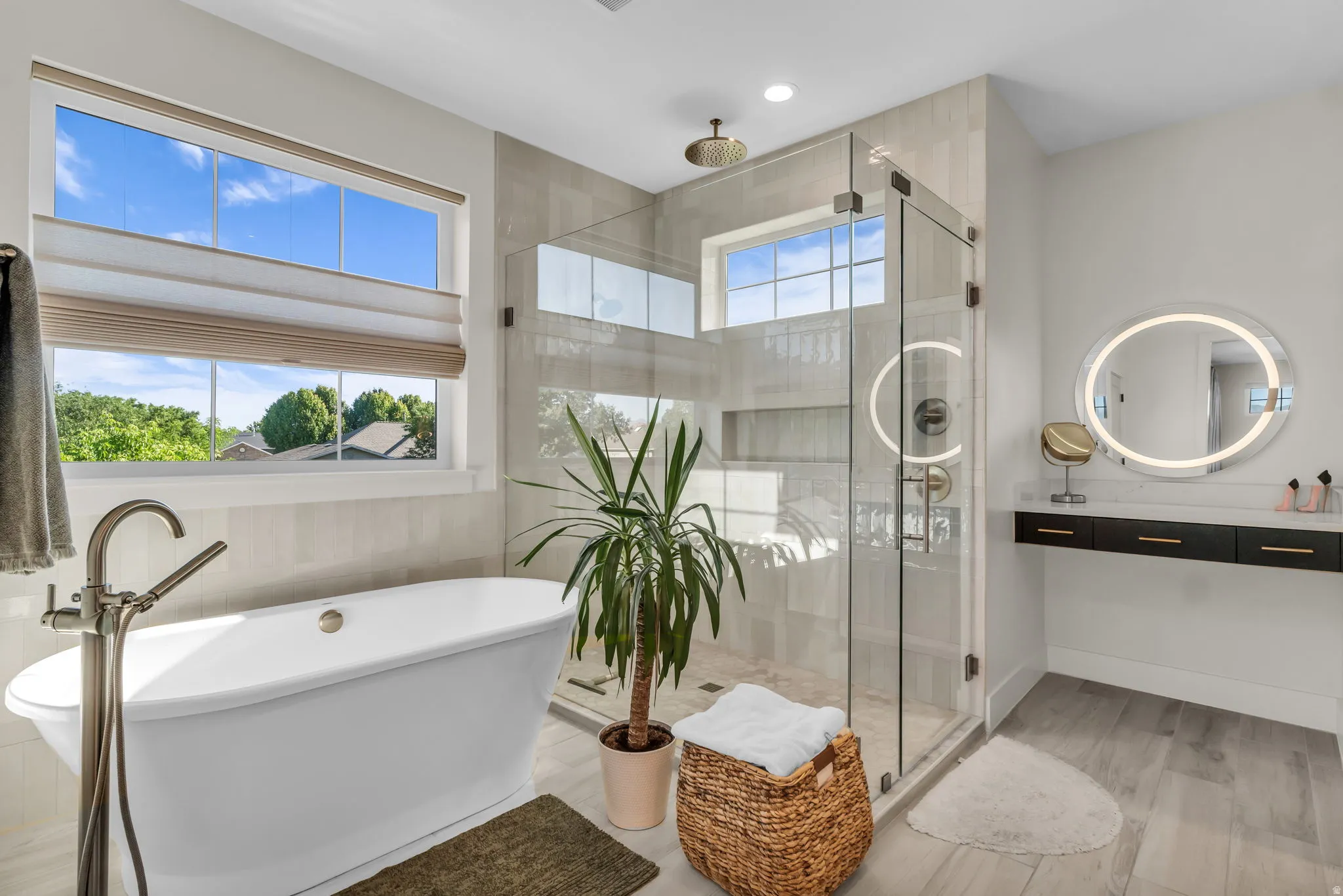 Contemporary bathroom featuring a freestanding tub with a floor-mounted faucet, a glass-enclosed shower with a rain showerhead, a floating vanity with integrated lighting, and wood-finish flooring