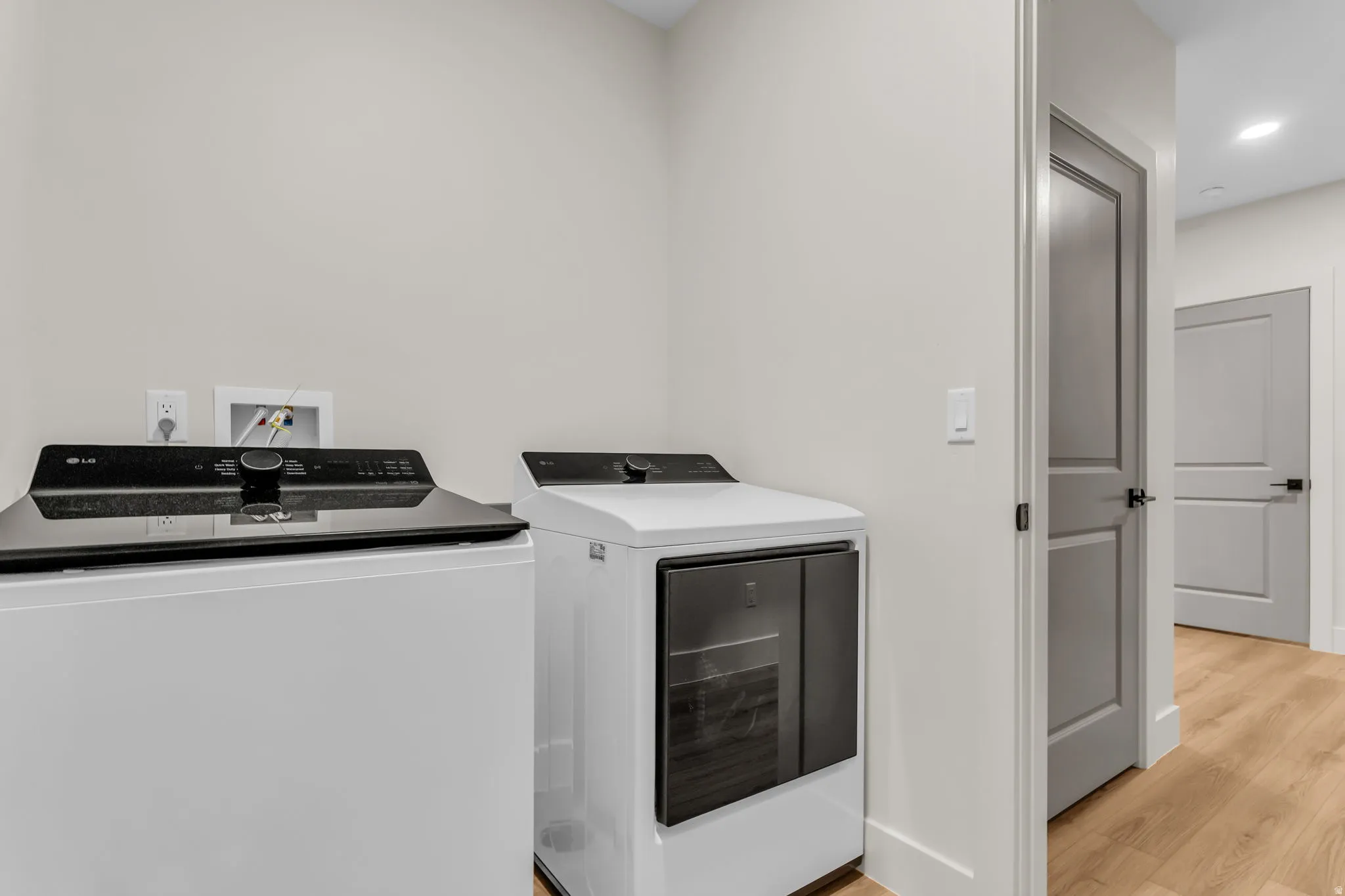Laundry area featuring light-toned walls, wood-finish flooring, and two contemporary appliances