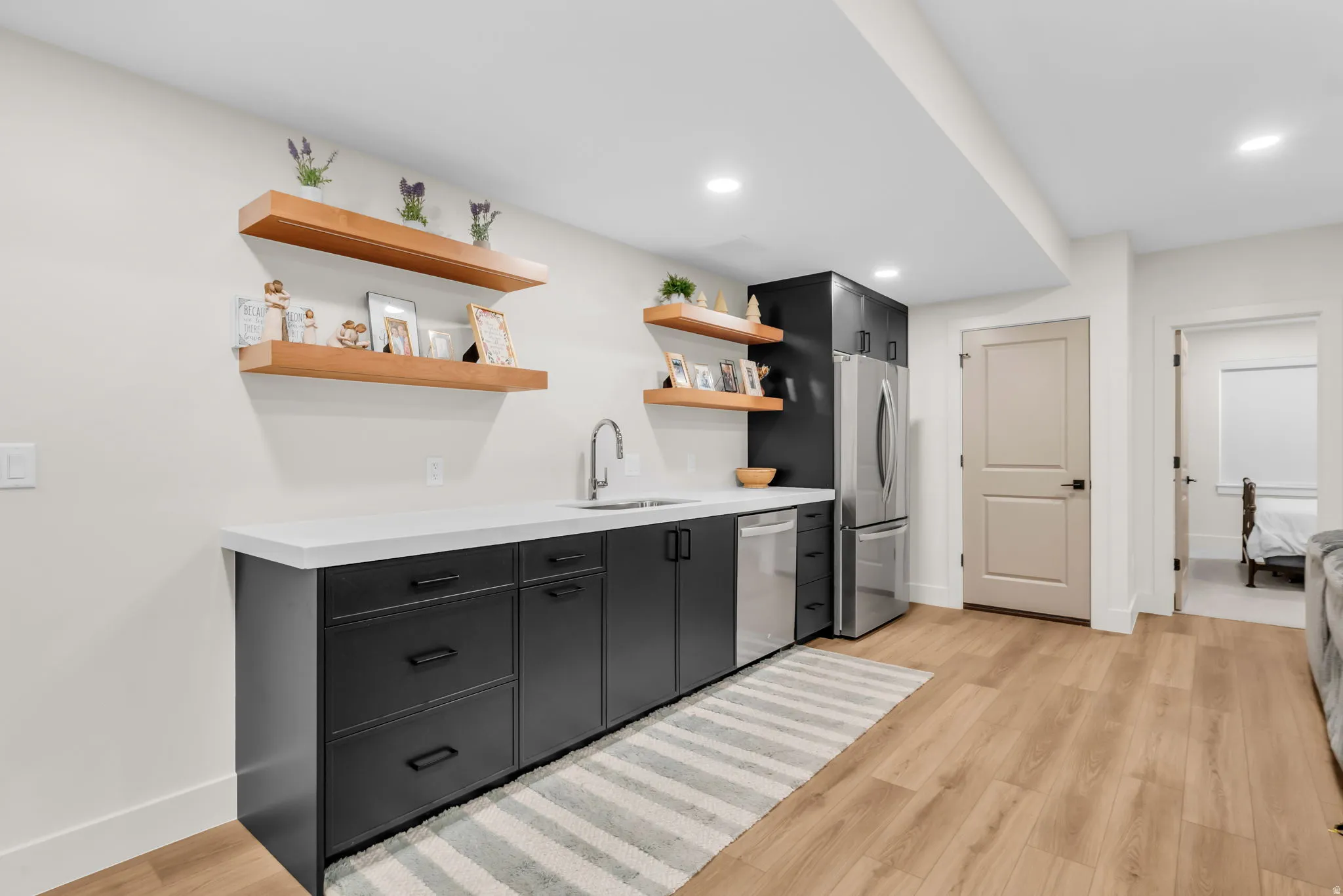Contemporary wet bar featuring matte black cabinetry, light-toned countertops, and wood-finish open shelving