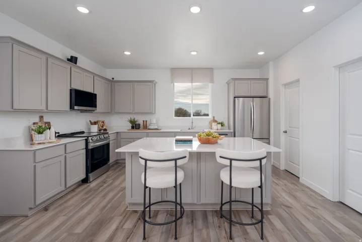 Bright kitchen featuring light gray cabinetry, white countertops, stainless steel appliances, and wood-finish flooring