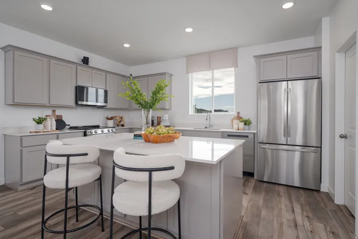 Kitchen featuring an island with countertop seating, light grey cabinetry, stainless steel appliances, a window with natural light, and wood-finish flooring