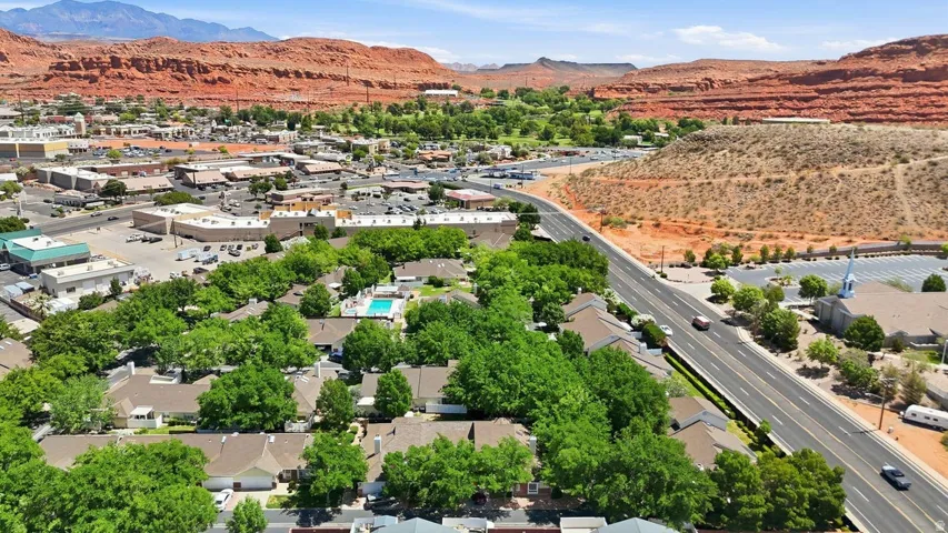 Residential community with mature tree cover and a central swimming pool, surrounded by commercial establishments and natural red rock formations