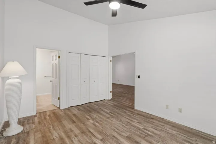 Spacious room featuring wood-finish flooring, crisp white walls, and a ceiling fan with integrated lighting