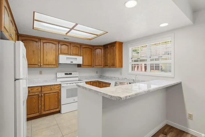 Kitchen featuring wood cabinetry, white appliances, speckled countertops, and a skylight