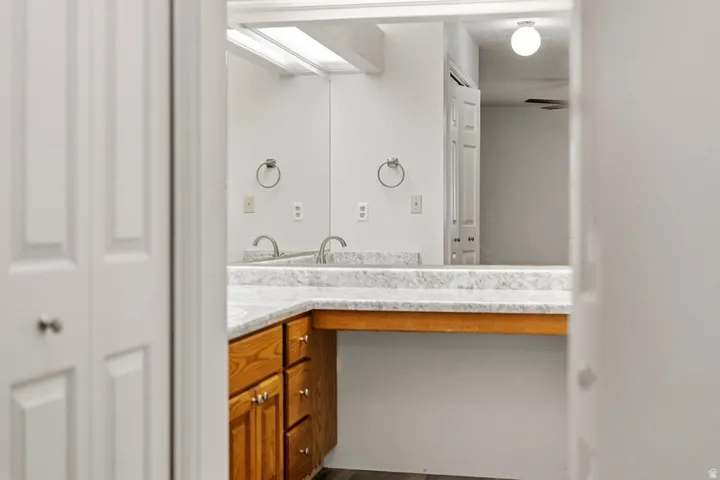 Vanity area featuring dual sinks, a large mirror, wood-finish cabinetry, and a light-toned countertop