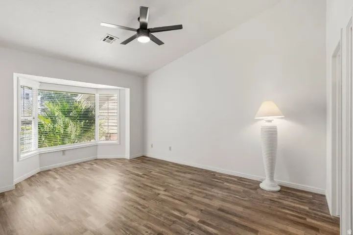 Bay window with privacy blinds, vaulted ceiling, wood-finish flooring, and a modern ceiling fan