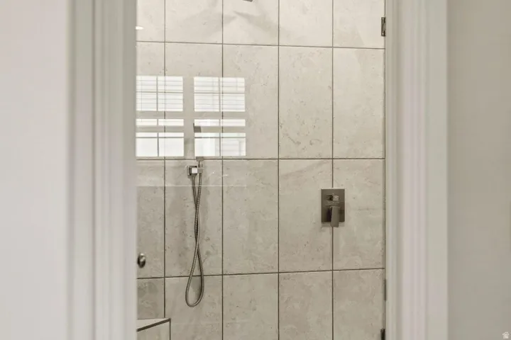 Glass-enclosed shower featuring large format wall tiles, a built-in shower niche, and a matte finish shower fixture with a handheld sprayer