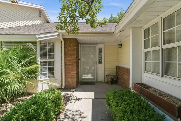 Front entrance featuring a concrete walkway, established shrubbery, a wood-finish planter box, brick accents, and a covered porch
