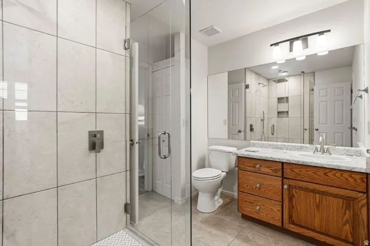 Bathroom featuring a glass-enclosed shower with large format tile, a vanity with wood cabinetry and a light-colored countertop, and a wide mirror