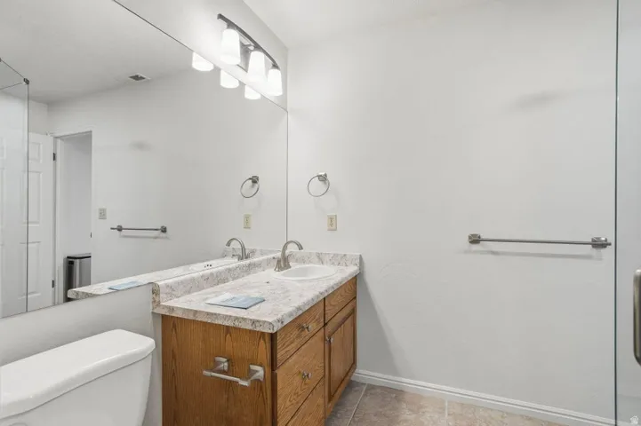 Bathroom vanity featuring a light wood-finish cabinet with brushed nickel pulls, a laminate countertop with an integrated sink, and an expansive wall-mounted mirror