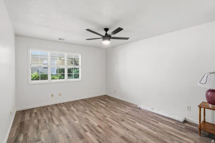 Spacious room featuring wood-finish flooring, a large window with white blinds, a ceiling fan with integrated lighting, and white painted walls