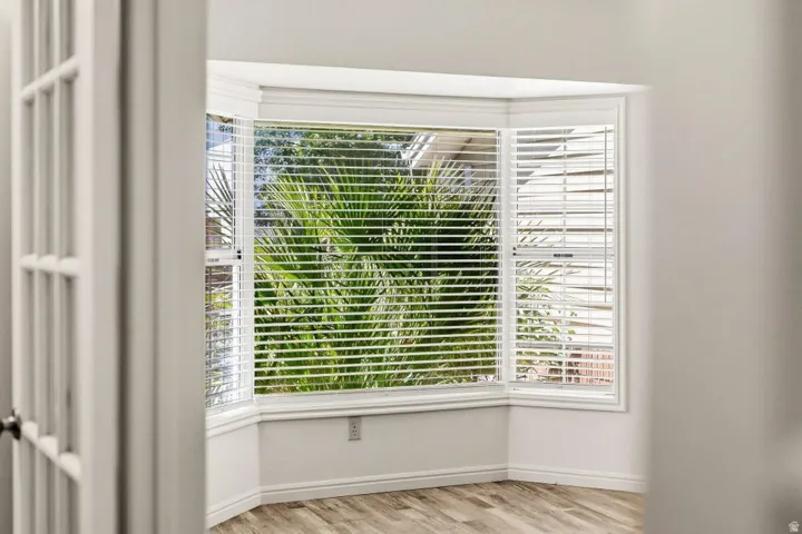 Bay window with louvered blinds, wood-finish flooring, white baseboards, and bright white walls
