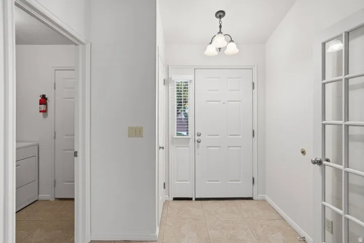 Foyer featuring a paneled entry door, tiled flooring, side window with blinds, and a three-light chandelier