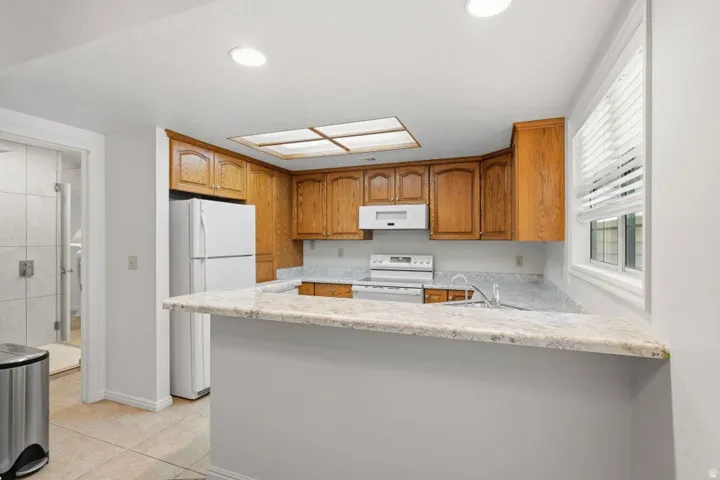 Kitchen featuring wood cabinetry, white appliances, a light-toned countertop, and recessed lighting