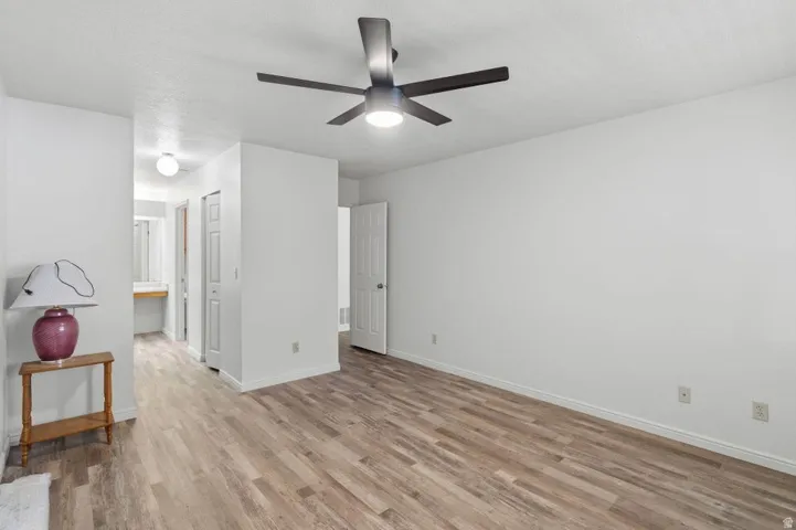 Spacious interior room featuring wood-finish flooring, white walls, and a contemporary ceiling fan with integrated lighting
