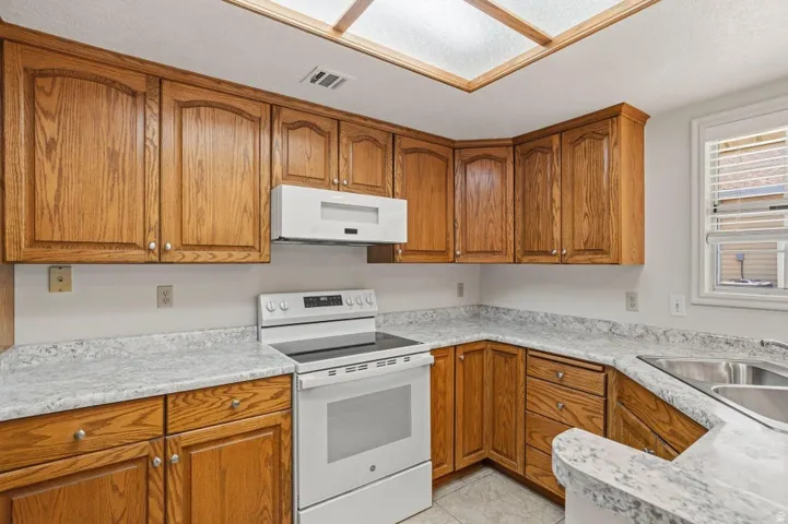 Kitchen featuring wood cabinetry, light-toned countertops, a white electric range, and a dual basin stainless steel sink