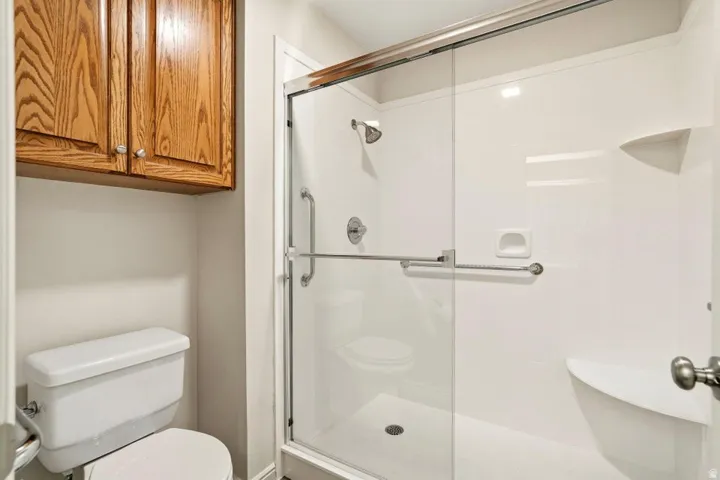 White shower enclosure with clear glass door, chrome fixtures, and built-in shelving