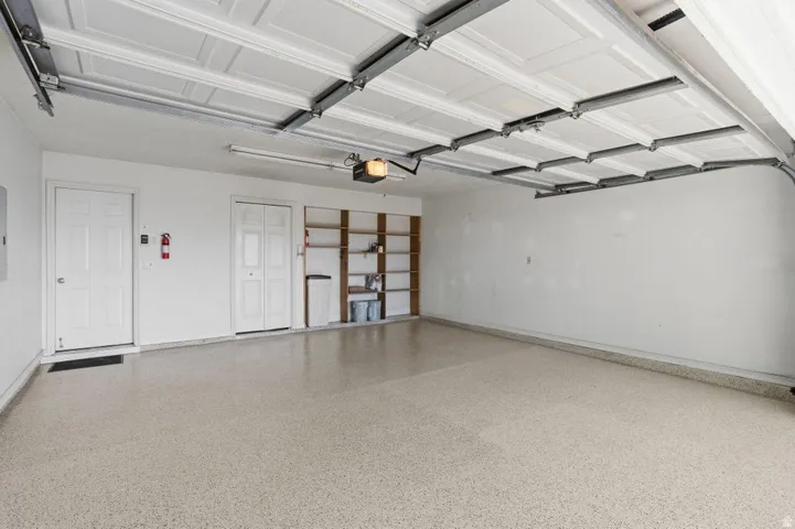Spacious garage featuring a durable speckled epoxy floor finish, overhead lighting, and built-in shelving for organized storage