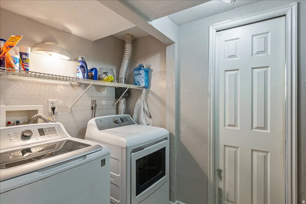 Utility room featuring a white paneled door, overhead lighting, and an overhead wire storage shelf