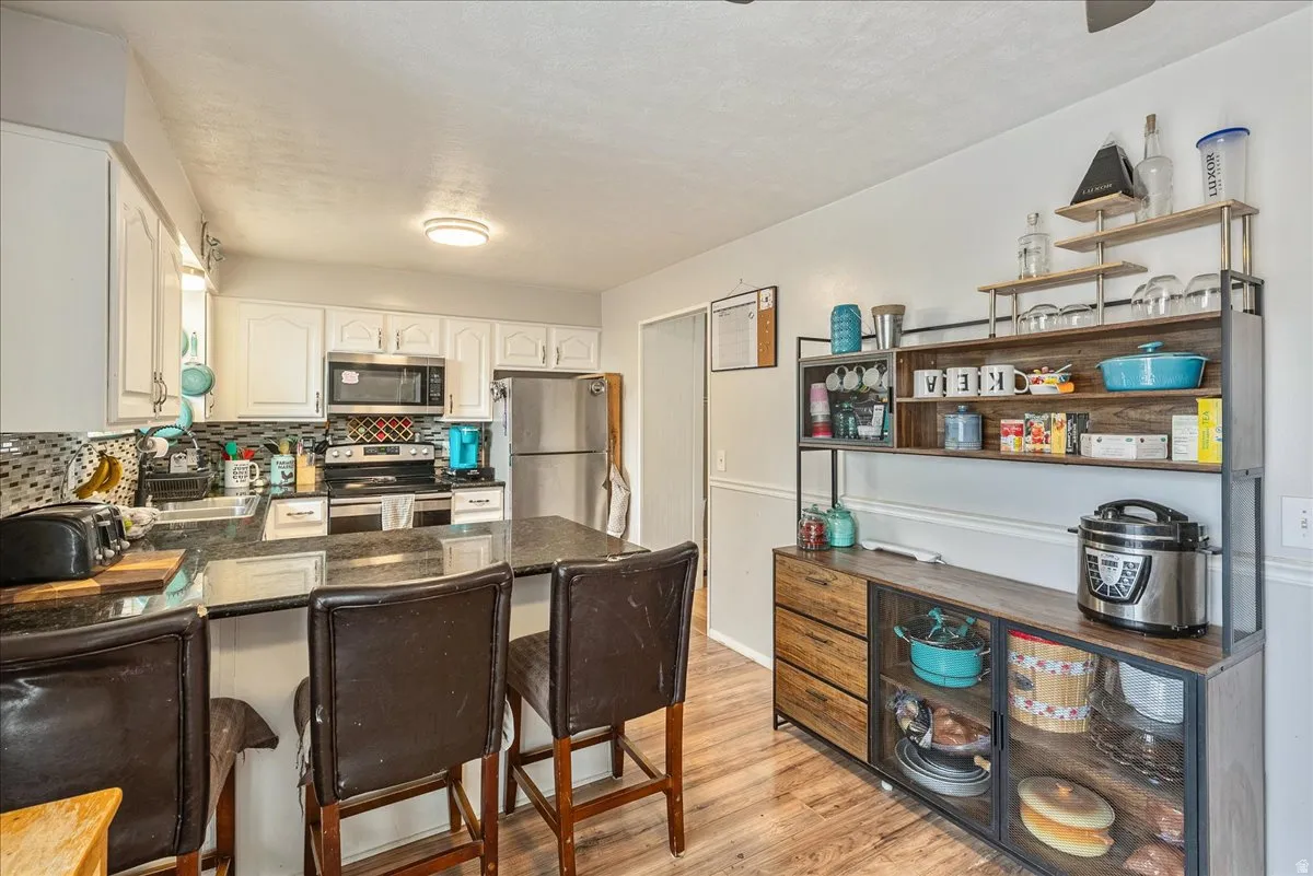 Kitchen featuring dark countertops, white cabinetry, stainless steel appliances, and a mosaic tile backsplash