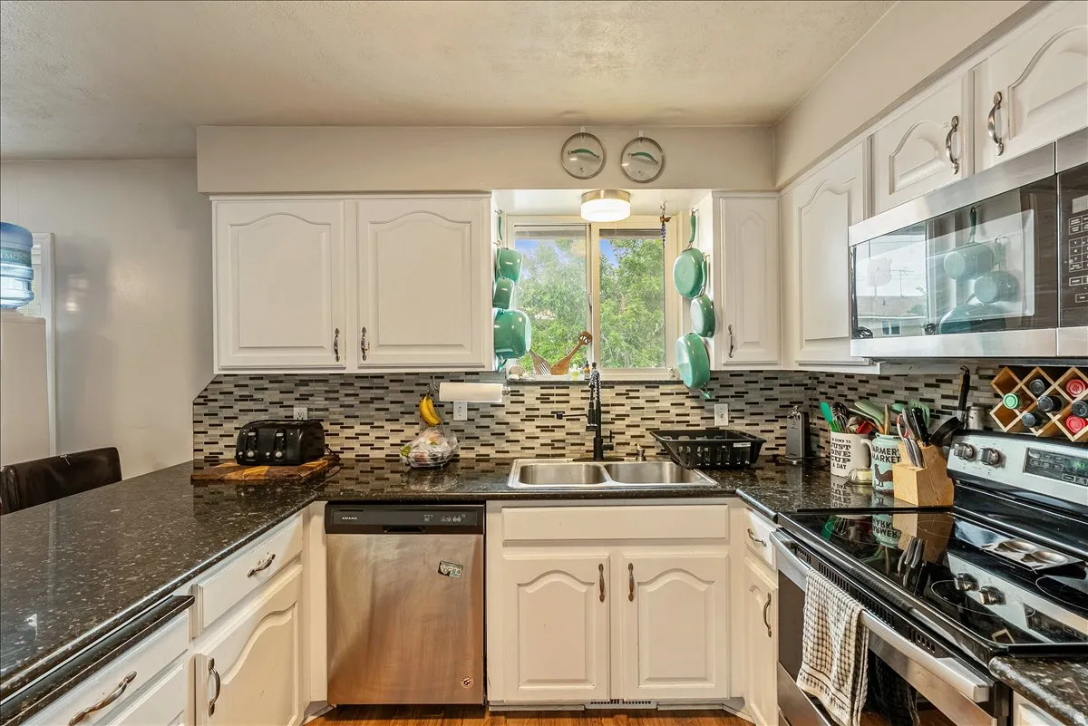 Kitchen featuring white cabinetry, dark speckled countertops, and a mosaic tile backsplash