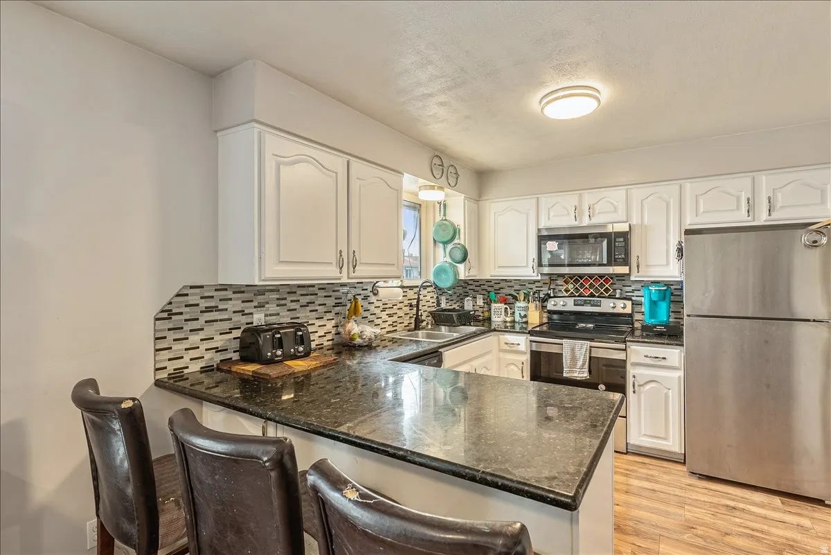 Kitchen featuring white cabinetry with brushed nickel hardware, stainless steel appliances, and a dark stone-finish countertop