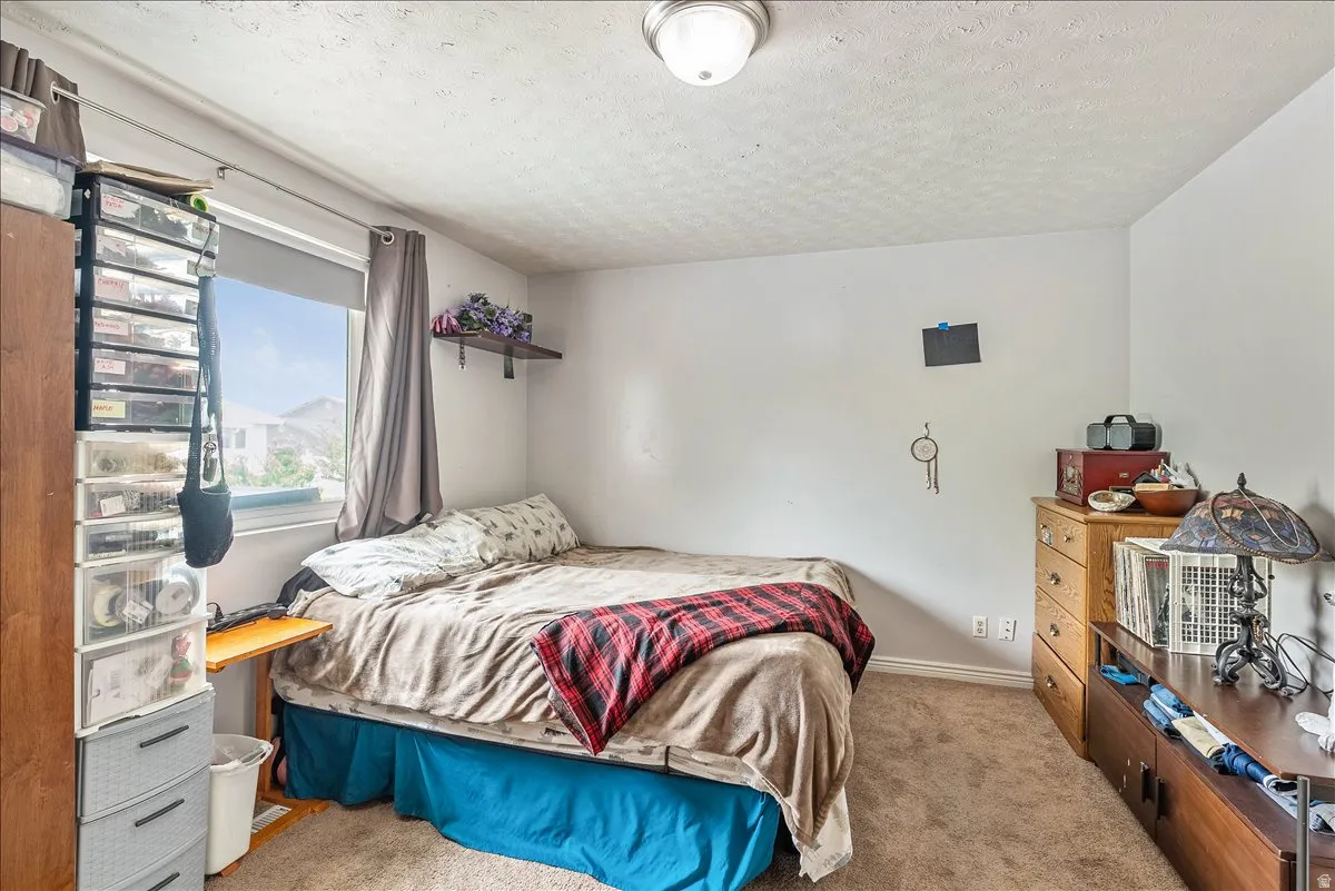 Bedroom featuring neutral wall paint, textured ceiling, a window with roller blind, and brown carpeting