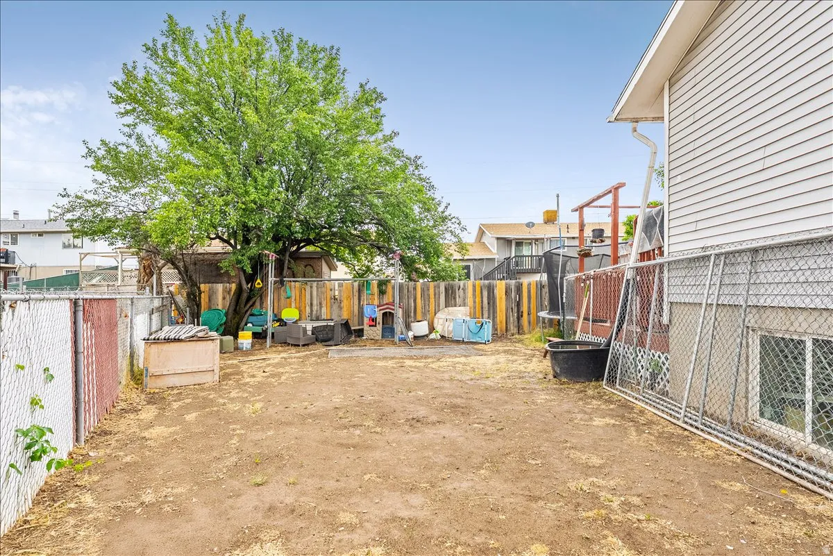 Expansive backyard featuring a mature deciduous tree, chain link fencing, a wood privacy fence, and a white siding exterior with a window
