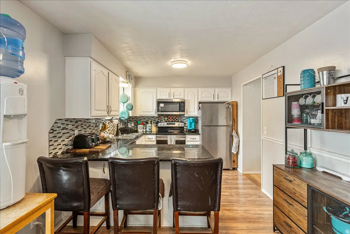 Kitchen featuring white cabinetry, dark stone countertops, stainless steel appliances, a tiled backsplash, and wood-finish flooring