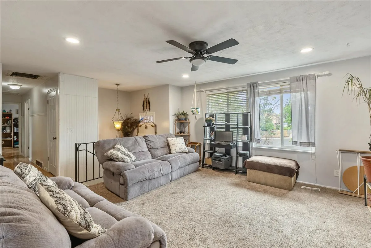 Carpeted living area featuring a ceiling fan with integrated lighting, recessed lighting, and a large window with blinds