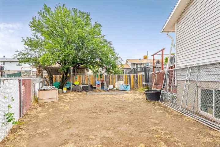 Expansive backyard featuring a mature deciduous tree, chain link fencing, a wood privacy fence, and a white siding exterior with a window
