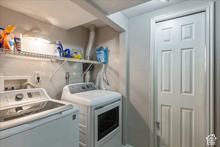 Utility room featuring a white paneled door, overhead lighting, and an overhead wire storage shelf