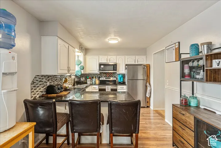 Kitchen featuring white cabinetry, dark stone countertops, stainless steel appliances, a tiled backsplash, and wood-finish flooring