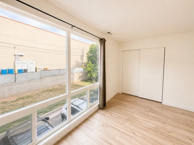 Bright room featuring large multi-panel windows, wood-finish flooring, white walls, and a built-in closet with sliding doors