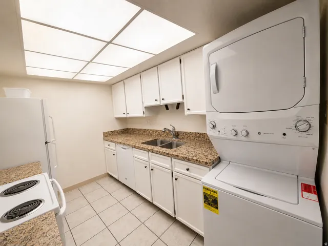Kitchen area featuring a stacked washer and dryer unit, white cabinetry, granite-finish countertops, and tile flooring