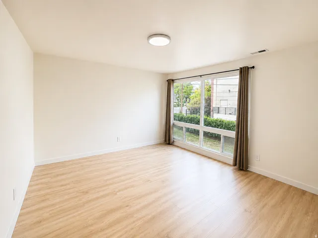 Spacious room featuring wood-finish flooring, white baseboards, and a large window with vertical panes