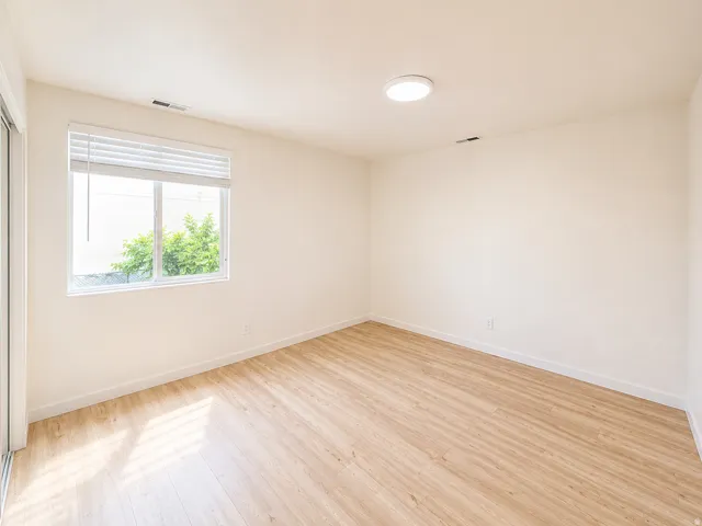 Bright room featuring wood-finish flooring, a large window with blinds, a sleek ceiling light fixture, white baseboards, and neutral wall paint