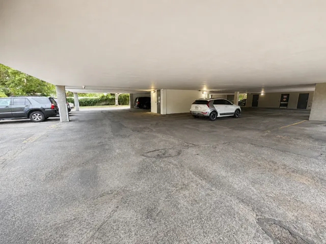 Covered parking area featuring concrete pillars, paved surface, and integrated overhead lighting