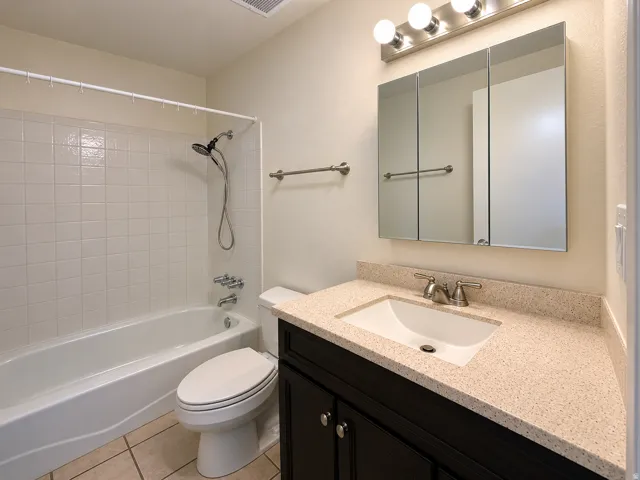 Bathroom featuring a dark wood vanity with a light speckled countertop, an undermount sink, a three-panel mirrored medicine cabinet, and a brushed nickel light fixture