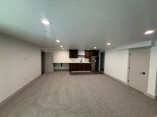 Spacious room featuring recessed lighting, a built-in kitchenette with dark wood-finish cabinetry, a stainless steel refrigerator, and a white countertop with an undermount sink