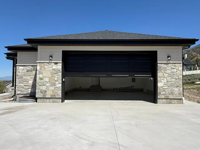 Two-car garage featuring a dark paneled door, stone facade, and concrete driveway