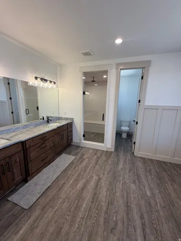 Bathroom featuring a dual vanity with a patterned countertop, rich wood-finish cabinetry, and a framed mirror