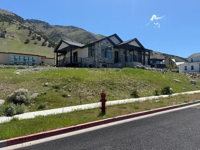 Modern mountain home featuring stone and siding exterior, large windows, an expansive covered porch with dark railings, and a hillside setting