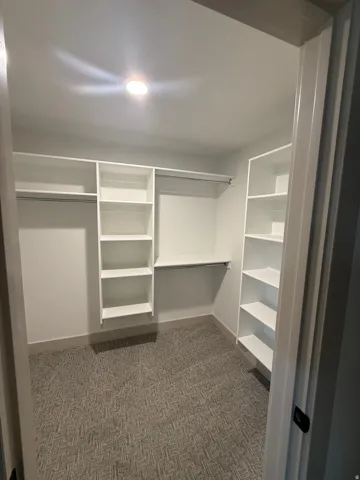 Walk-in closet featuring built-in white shelving, hanging rods, and patterned carpet flooring