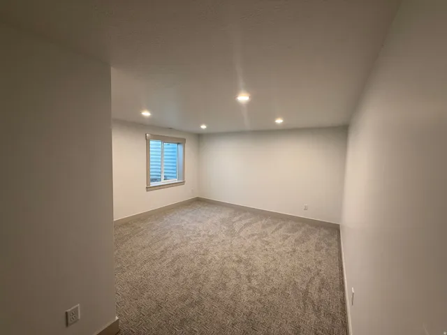 Spacious room featuring neutral carpeting, recessed ceiling lighting, and a window with white trim