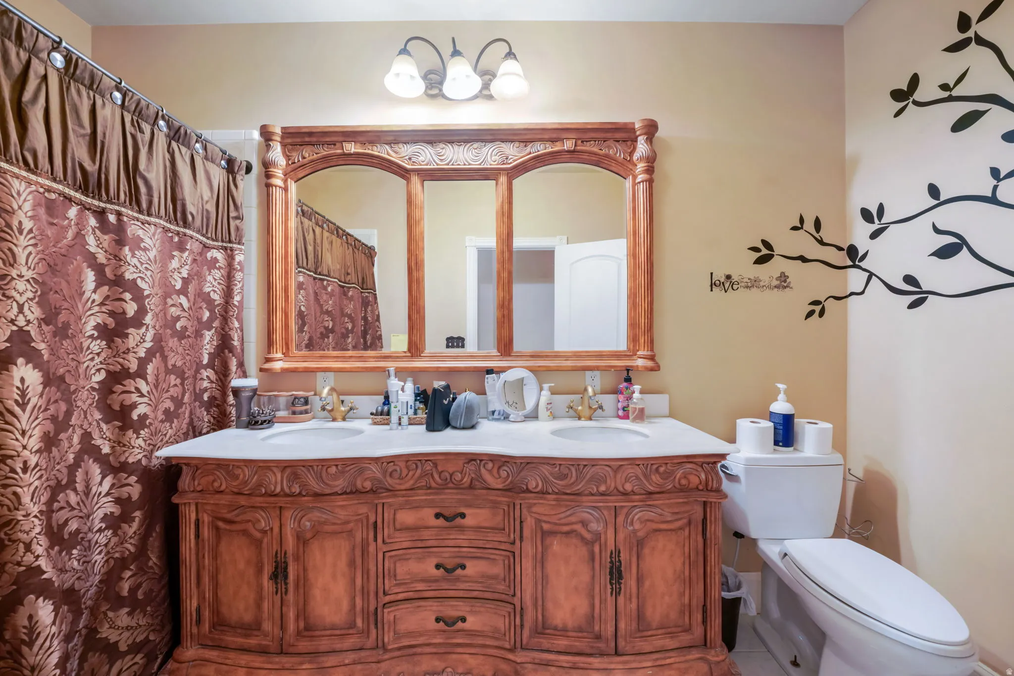 Main bathroom with double vanity featuring two integrated sinks set in a light-toned countertop, with an ornate wood-framed mirror above